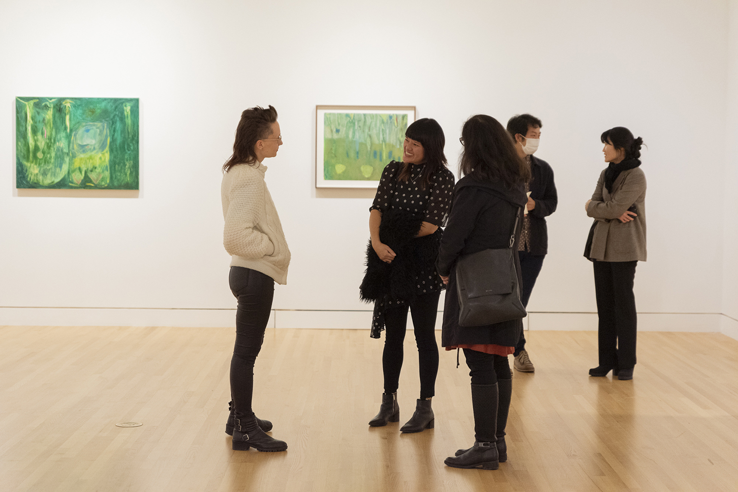 Five people standing in a gallery with white walls and two paintings